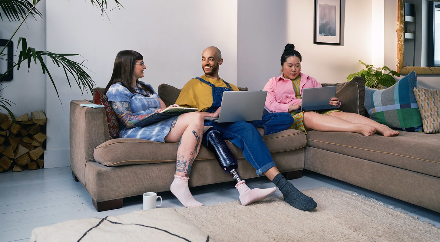 Three people sitting on a couch, each using a laptop, engaged in work or study together in a cozy setting.